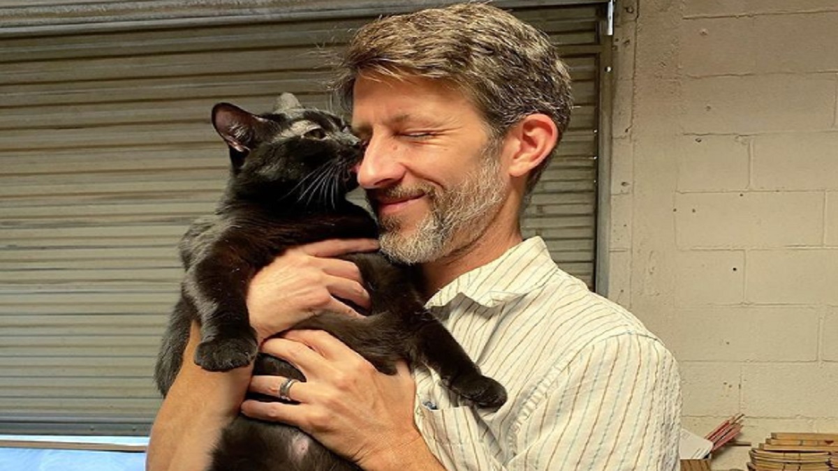 A black cat kisses a man on the nose.