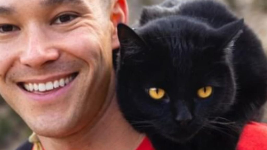 A black cat sitting on man's shoulder.